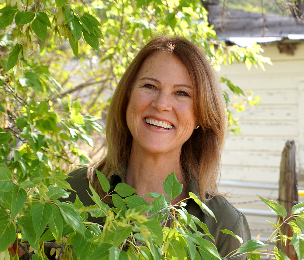 Audrey standing behind a tree with a white building in the background
